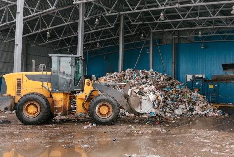 Yellow front loader moving a large pile of waste materials inside a facility, representing industrial product destruction processes.